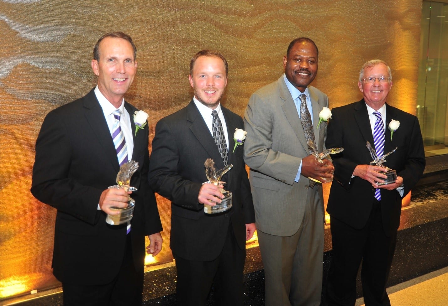 Four men in suits and ties holding trophies.
