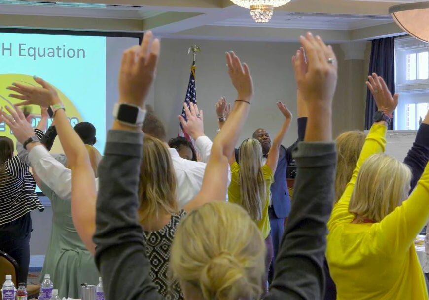 A group of people raising their hands in front of a projector screen.